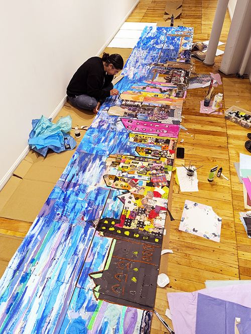 Alice Mizrachi sits on the floor to add details to the Minneapolis Skyline collage mural at the Davis Art Gallery.