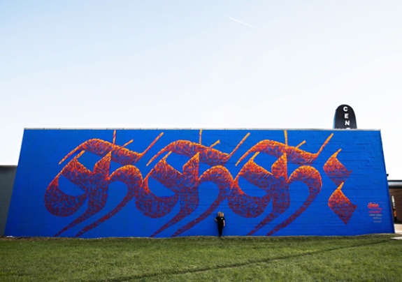 Mural by Sneha Shrestha (IMAGINE) titled Everybody Is Welcome (2019). Nepali letter repeated three times in orange and red on a blue background.