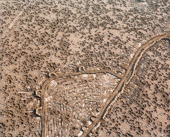 Photograph by Sophie Ristelhueber from the series FAIT (1992). Aerial view of a desert landscape filled with bomb craters.