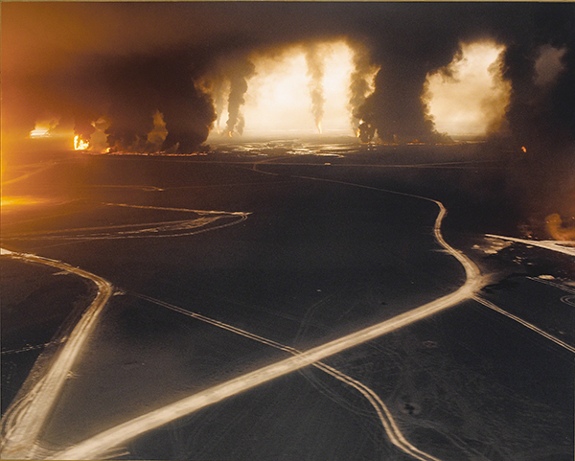 Photograph by Sophie Ristelhueber from the series FAIT (1992). Nighttime scene with glowing lines and tall plumes of smoke and fire in the distance.