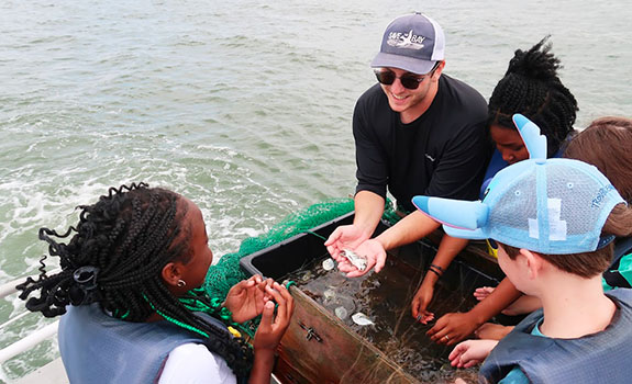 Students Drew J., Brayden H., and LeeʼAyla F. learn about local aquatic life from boat tour guide Josh Gilliland.