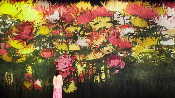 Installation by teamLab titled January from Proliferating Immense Life - A Whole Year per Year (2020). Woman standing in front of large yellow and pink flowers.